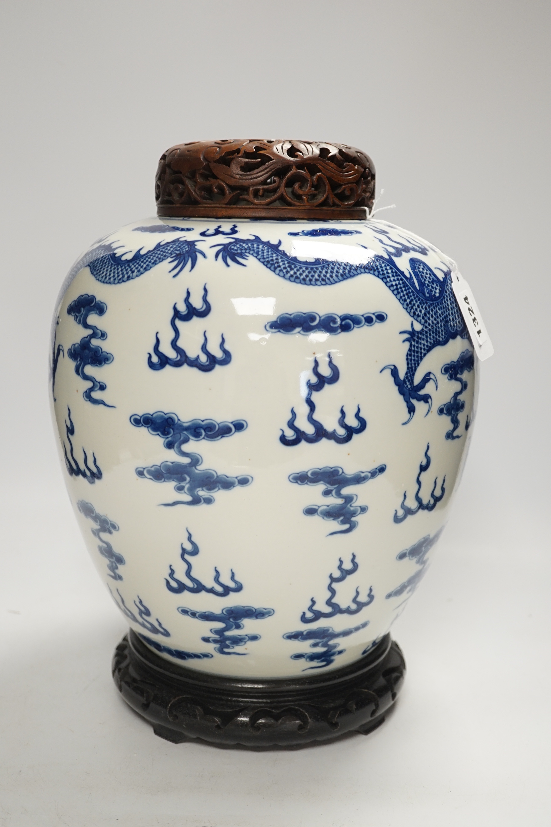 A large Chinese blue and white jar decorated with dragons chasing the flaming pearl together with unassociated carved wood lid and stand, 35cm high